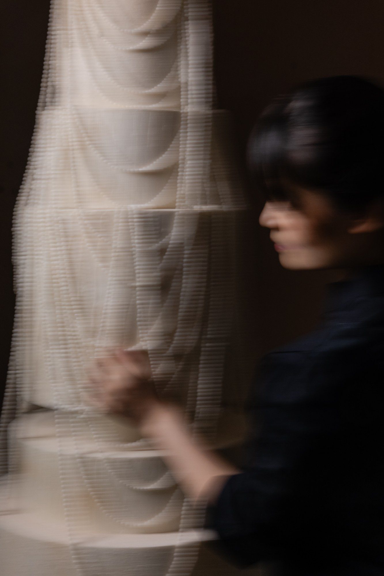 Fiona Lewy in motion beside a tall draped ivory wedding cake, in low light.