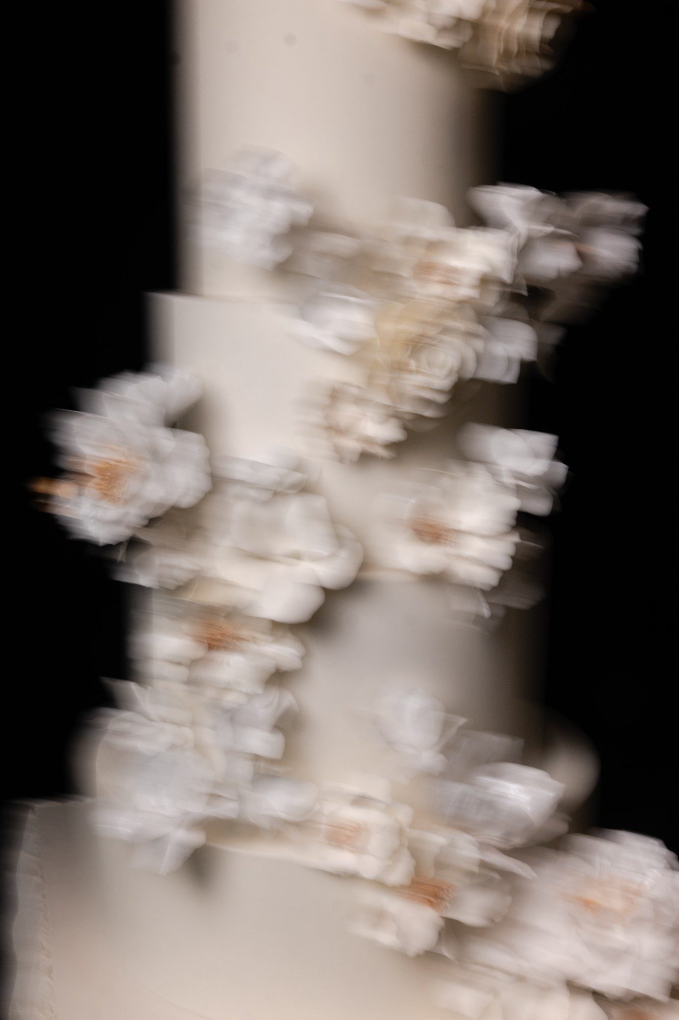 A close view of sugar flowers on an ivory wedding cake, blurred in motion.